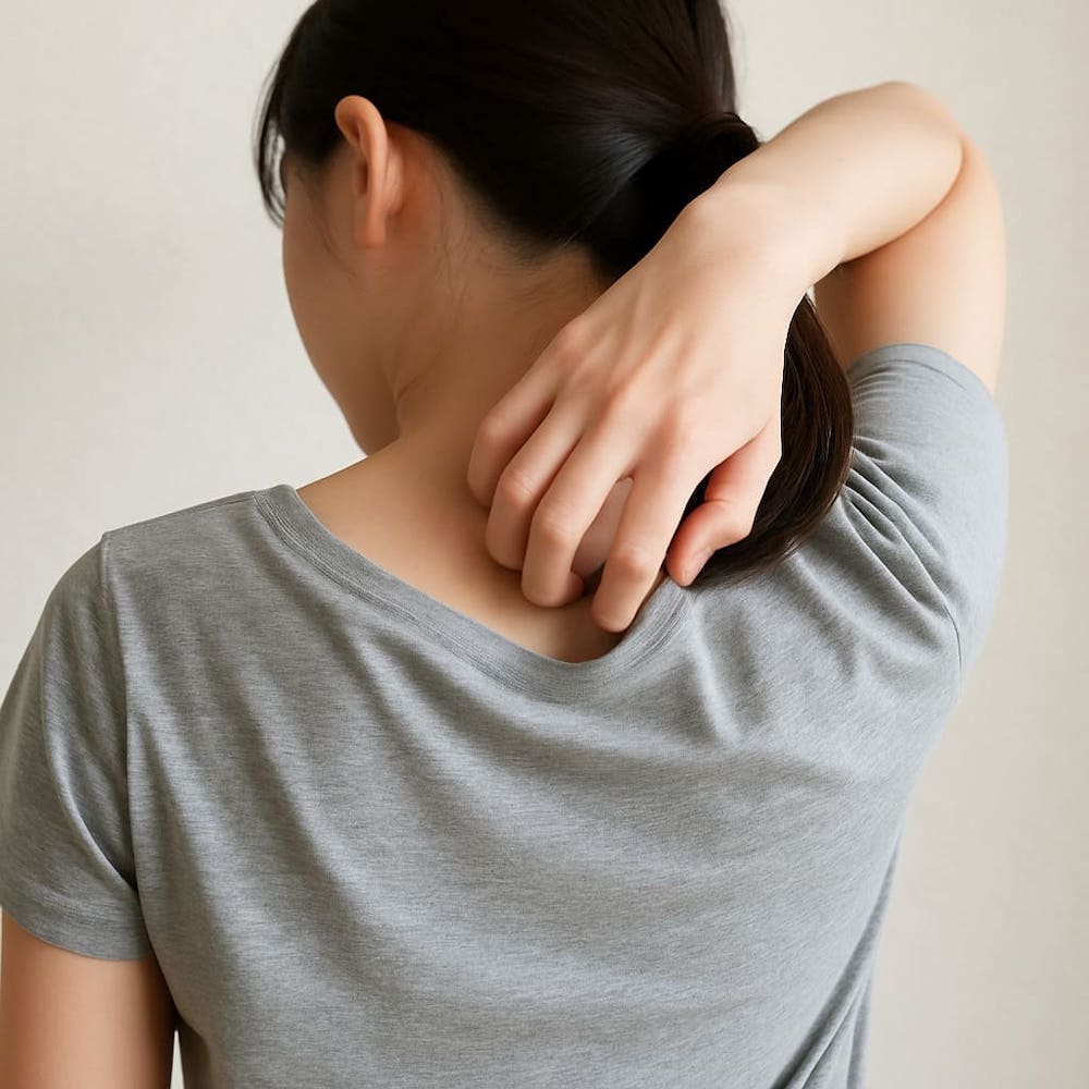 背中を向けた女性が、首の下あたりを右手で掻いている写真